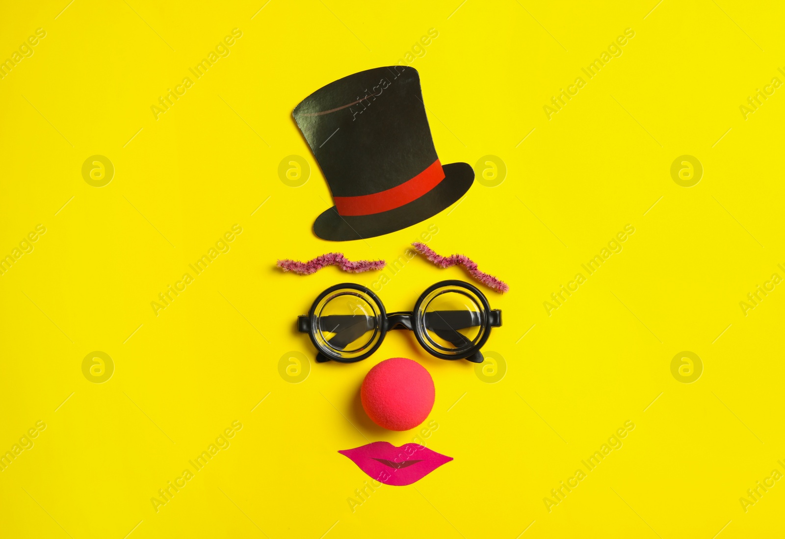 Photo of Funny face made with clown's accessories on yellow background, flat lay