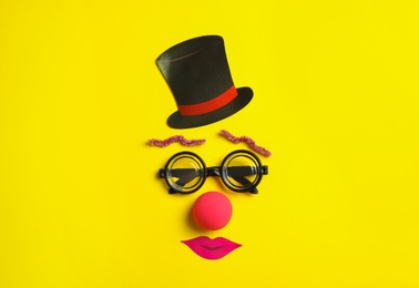 Funny face made with clown's accessories on yellow background, flat lay