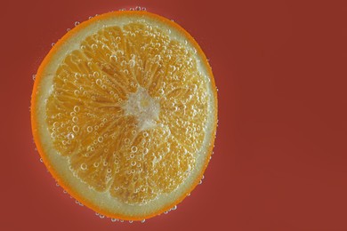 Photo of Fresh orange slice in sparkling water on red background. Space for text