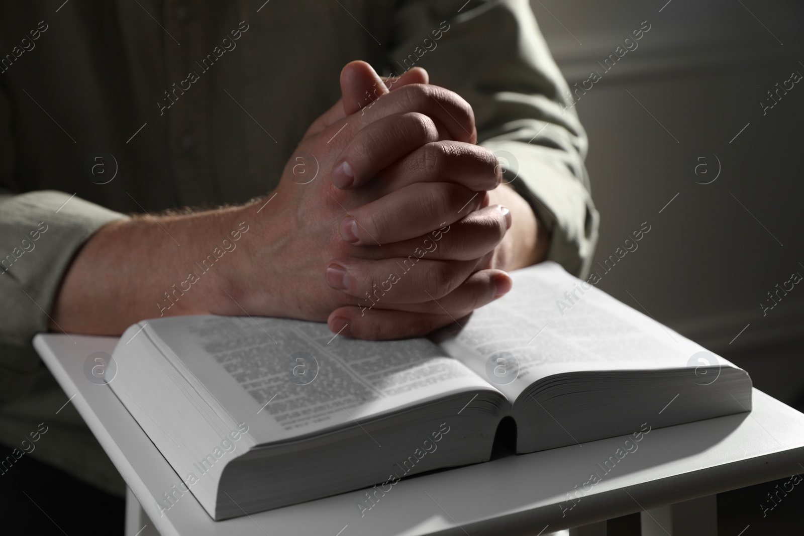 Photo of Religion. Christian man praying over Bible indoors, closeup