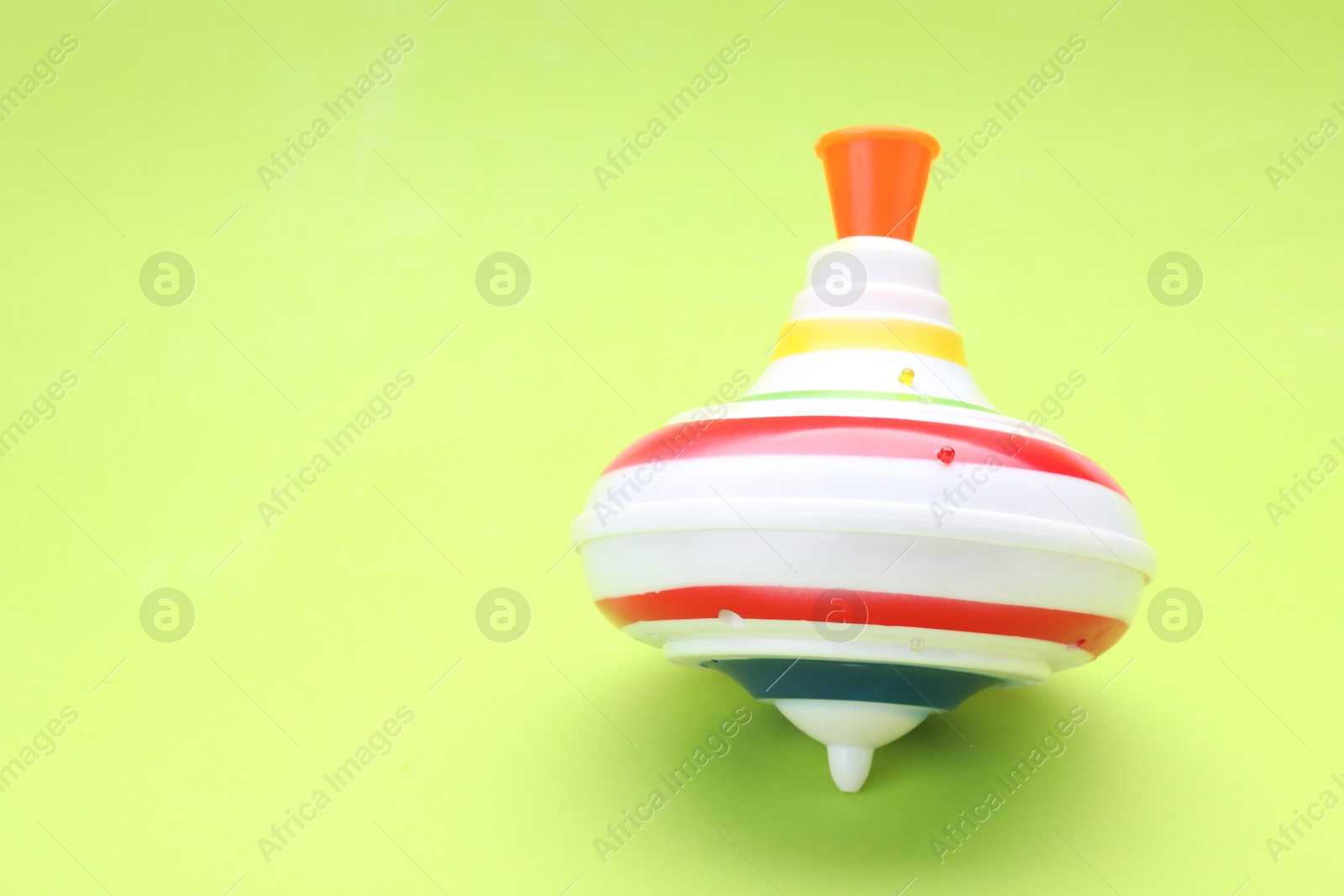 Photo of One bright spinning top on light green background, space for text. Toy whirligig