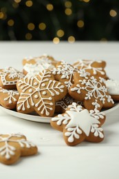 Photo of Tasty Christmas cookies with icing on white wooden table against blurred lights, closeup