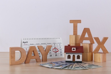 Photo of Phrase TAX DAY, wooden cubes, house model, calendar and money on table