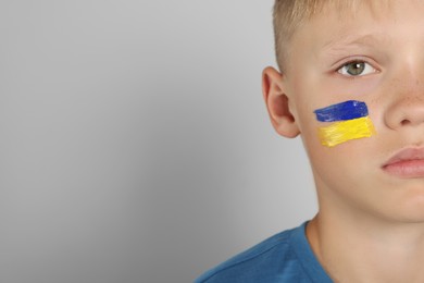 Photo of Little boy with drawing of Ukrainian flag on face against light grey background, space for text
