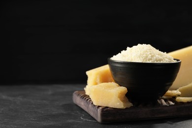 Photo of Bowl with grated parmesan cheese on table against black background. Space for text