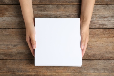 Woman holding blank paper sheets for brochure at wooden table, top view. Mock up