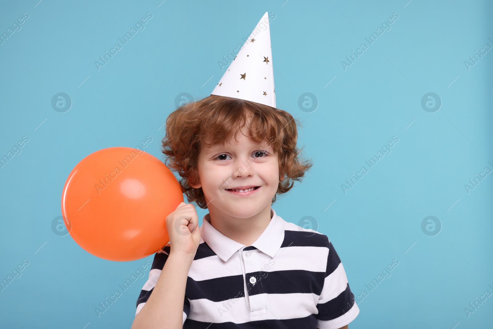 Photo of Happy little boy in party hat with balloon on light blue background