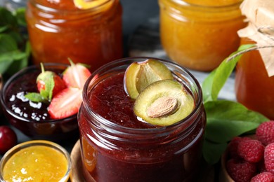 Photo of Jars with different jams and fresh fruits on table, closeup
