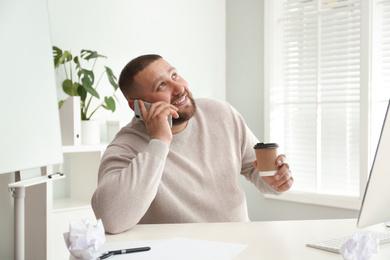 Photo of Lazy overweight office employee talking on phone at workplace