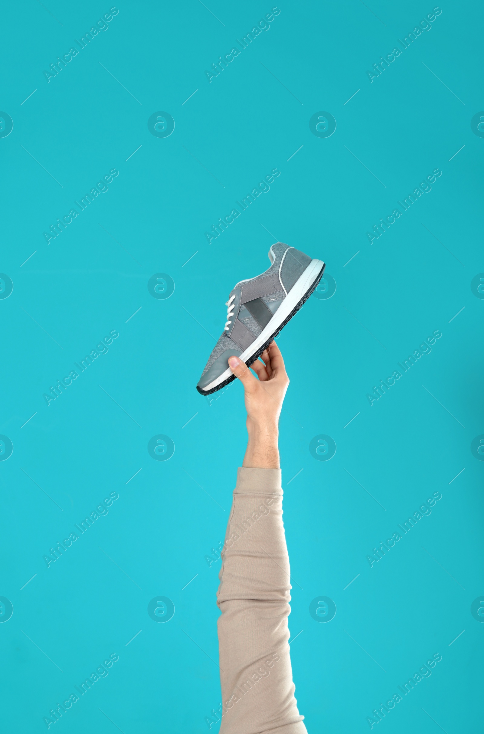 Photo of Young man holding comfortable shoe on light blue background, closeup