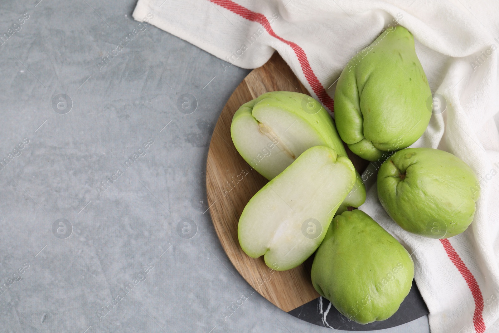 Photo of Cut and whole chayote on gray table, top view. Space for text