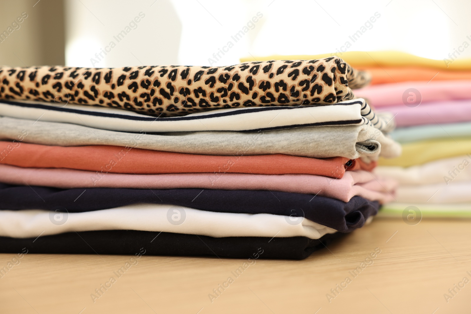 Photo of Many stacked clean clothes on wooden table, closeup