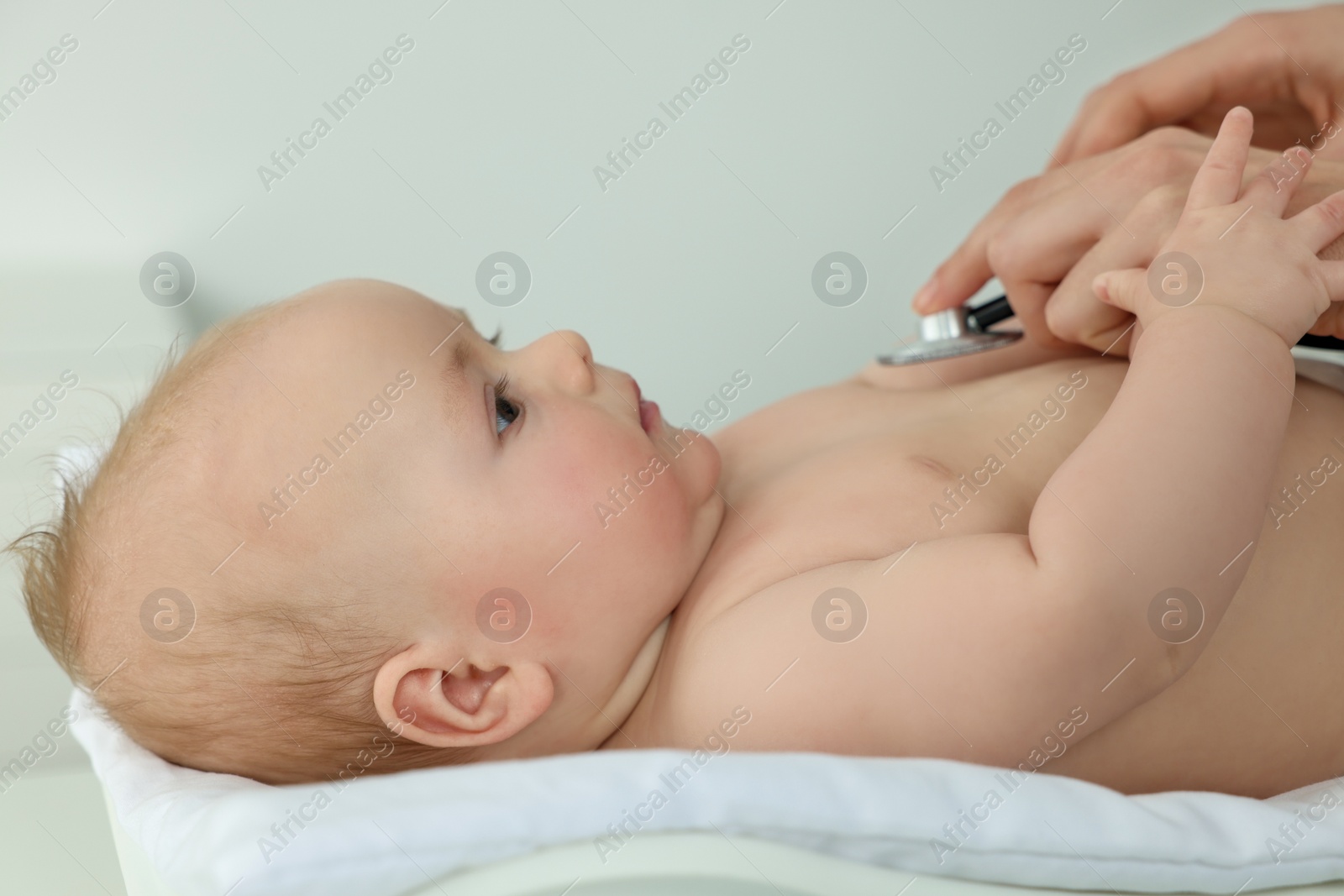 Photo of Pediatrician examining cute little baby with stethoscope in clinic, closeup