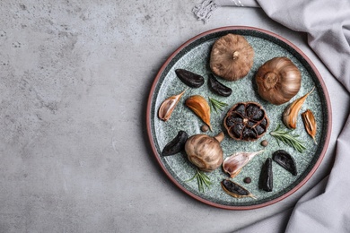 Plate with black garlic on grey table, top view. Space for text