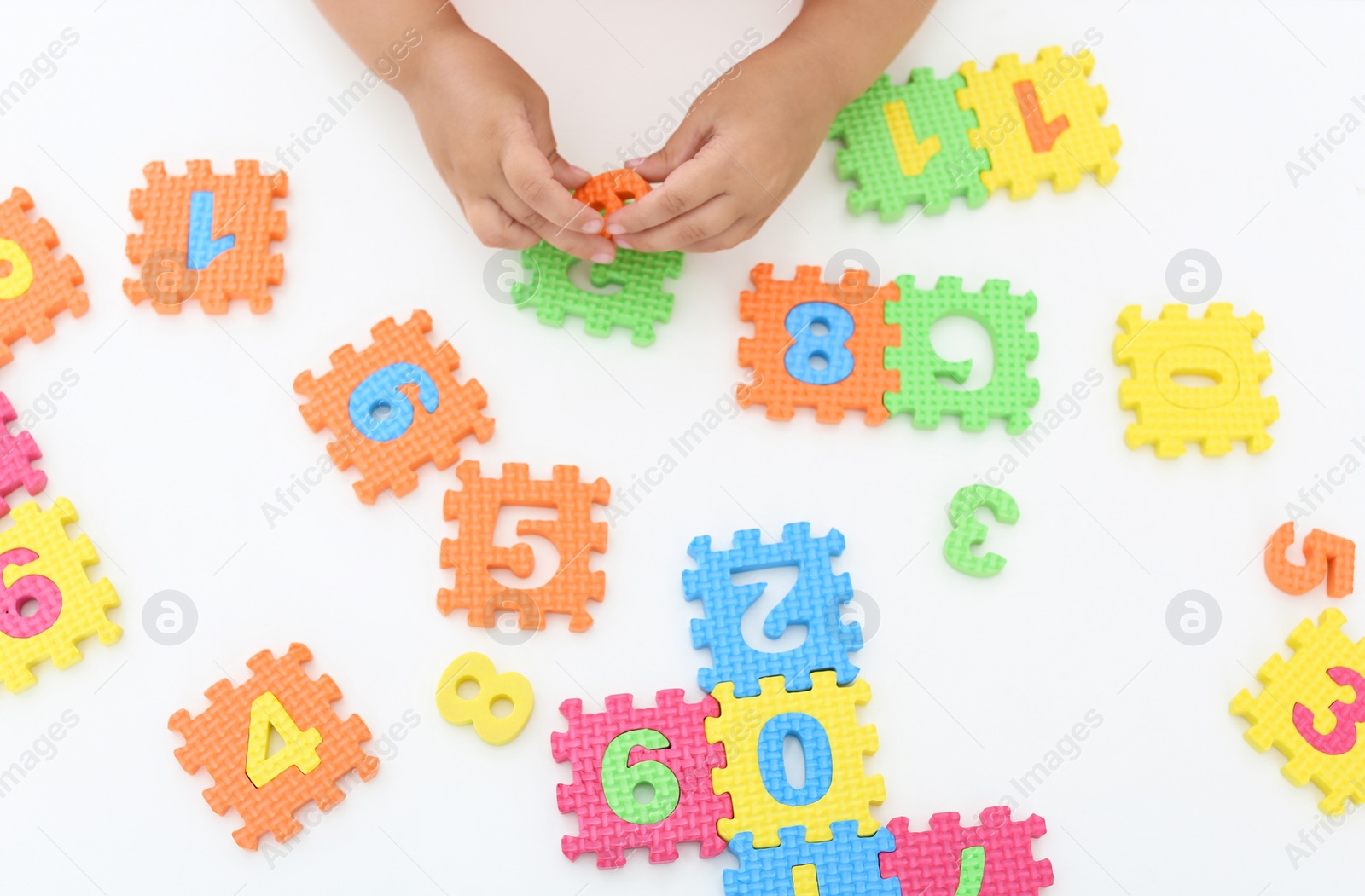 Photo of Little girl playing with colorful puzzles at white table, top view. Educational toy