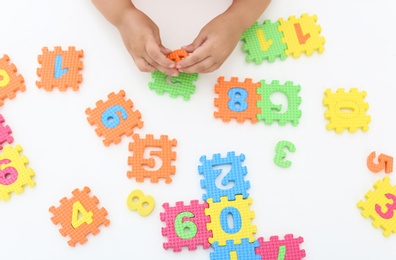 Little girl playing with colorful puzzles at white table, top view. Educational toy