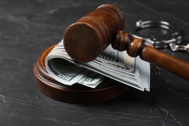 Photo of Judge's gavel, money and handcuffs on dark grey table, closeup