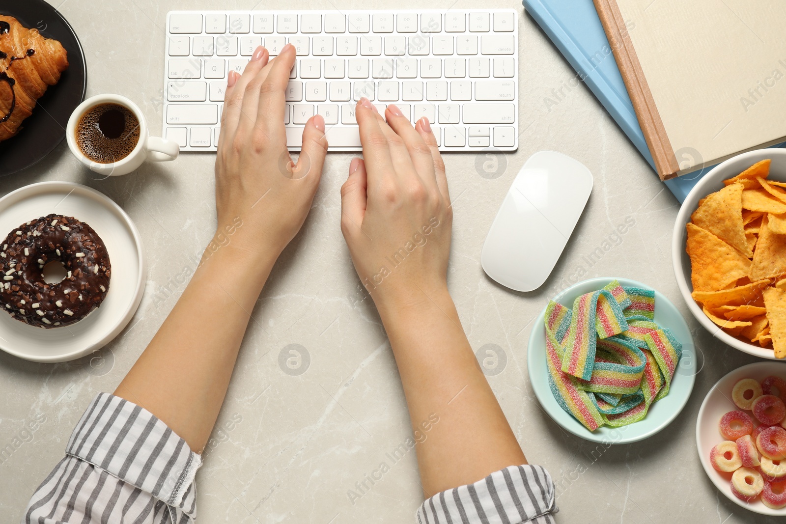 Photo of Bad eating habits. Woman working on computer at light grey marble table with different snacks, top view