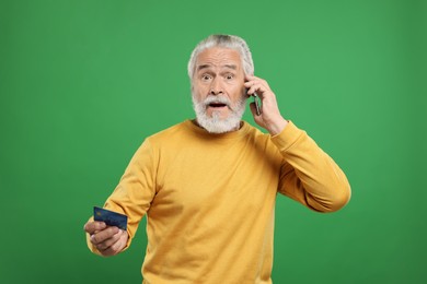 Photo of Shocked senior man with credit card talking on smartphone against green background. Be careful - fraud