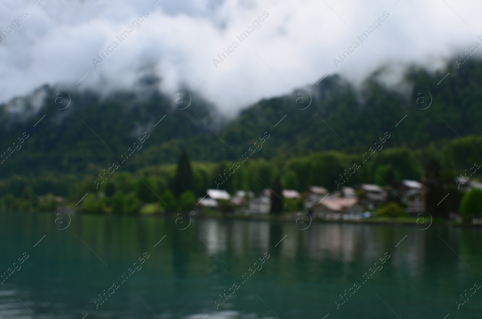 Photo of Blurred view of beautiful village on lake shore near mountains