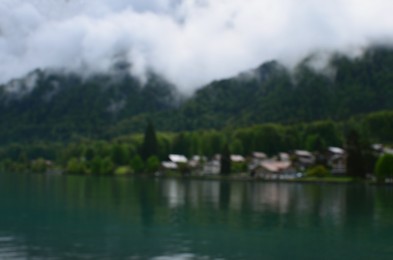 Photo of Blurred view of beautiful village on lake shore near mountains