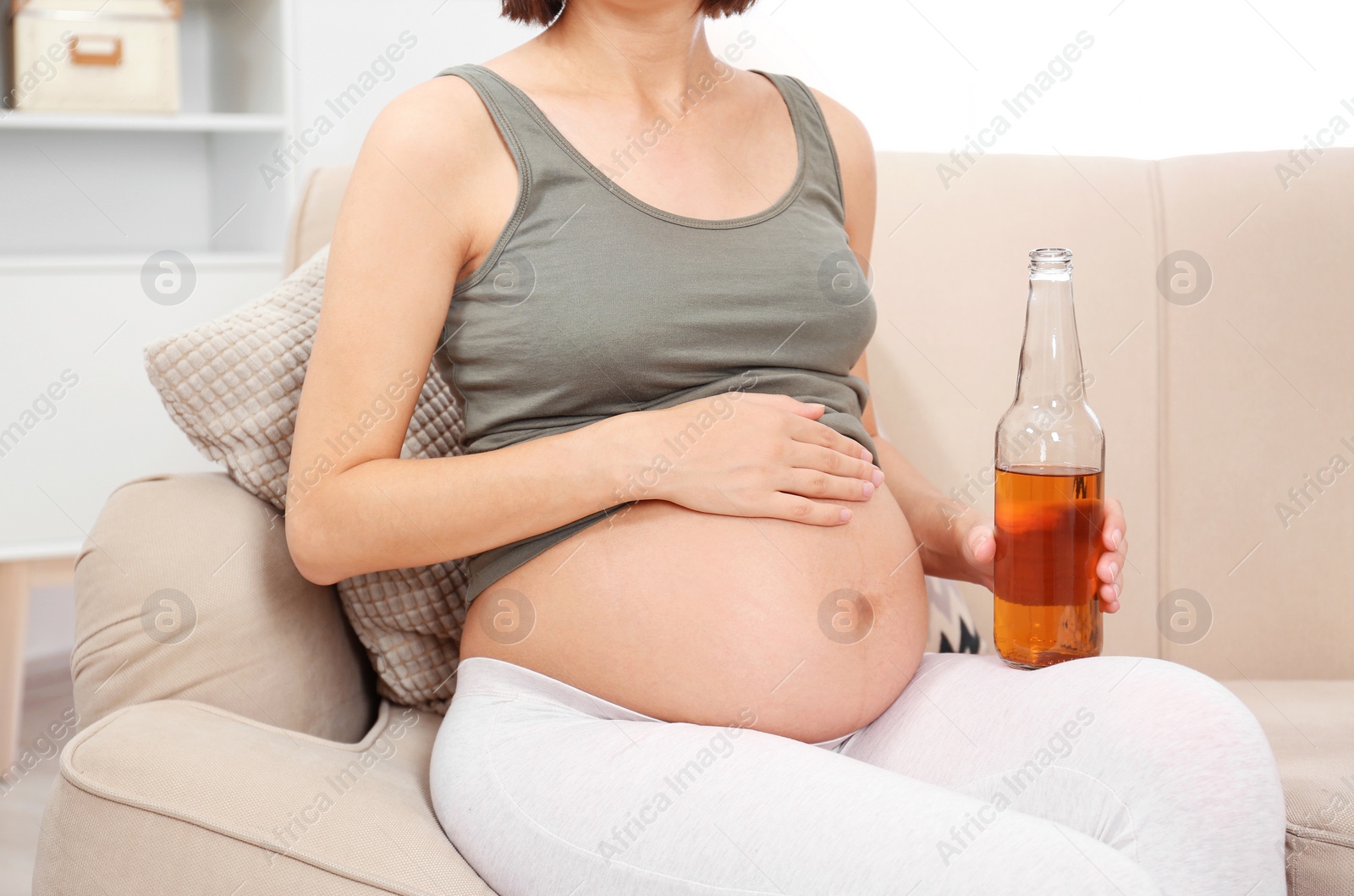 Photo of Pregnant woman with bottle of whiskey at home. Alcohol addiction