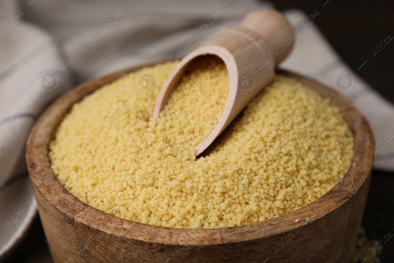 Photo of Bowl and scoop with raw couscous on table, closeup