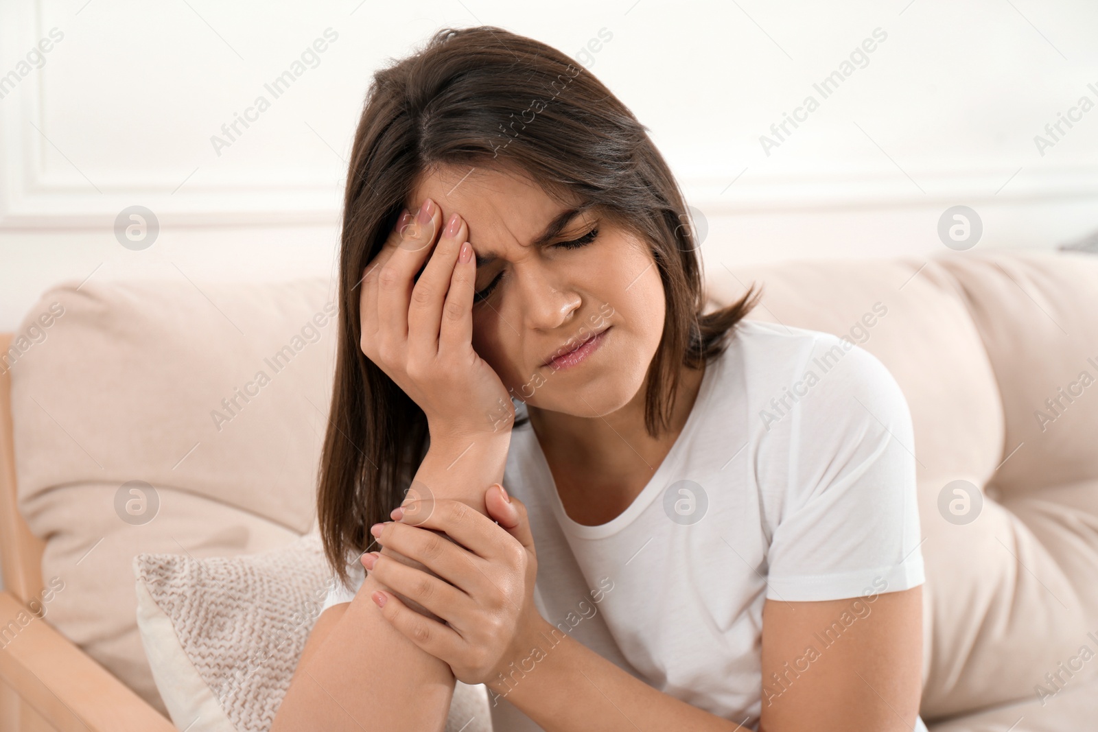 Photo of Young woman suffering from migraine on sofa at home