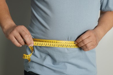 Photo of Man measuring waist with tape on grey background, closeup