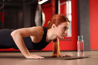 Photo of Athletic young woman doing push ups on mat in gym