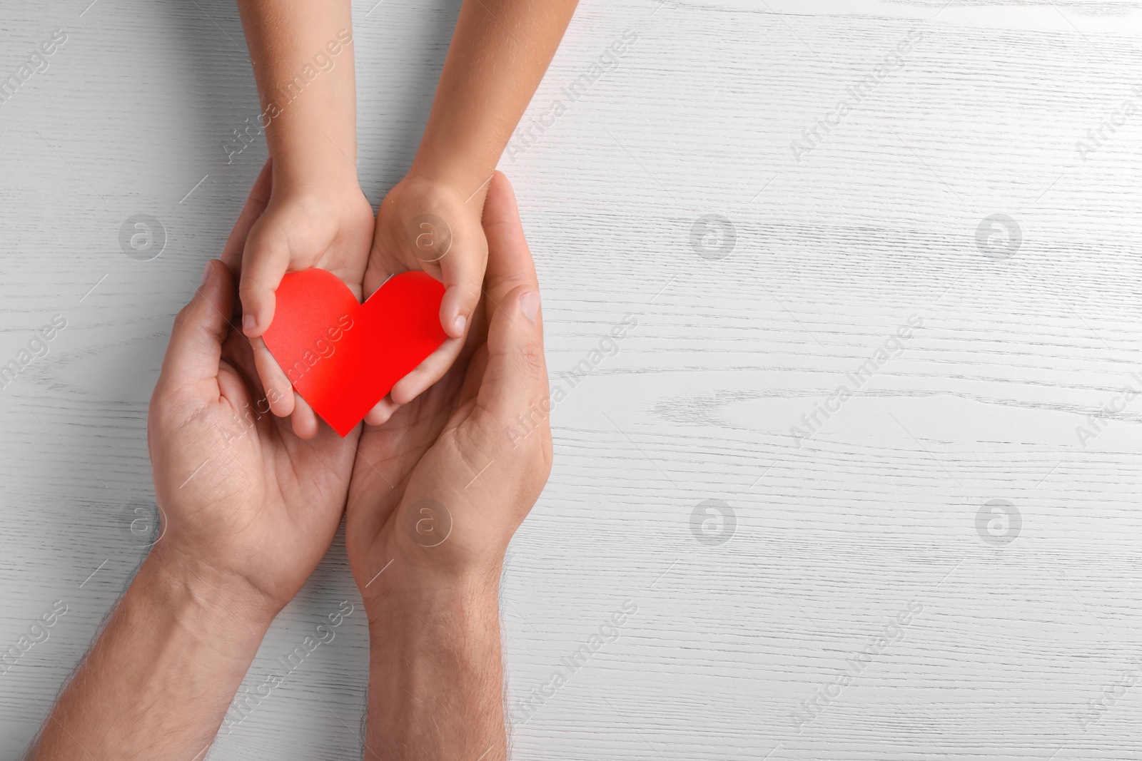 Photo of Family holding small red heart in hands on wooden background