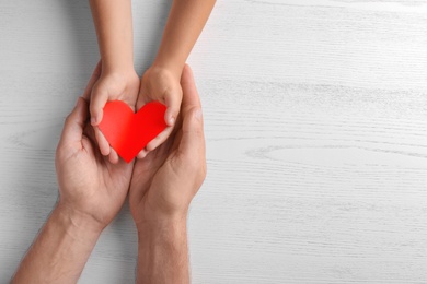 Photo of Family holding small red heart in hands on wooden background