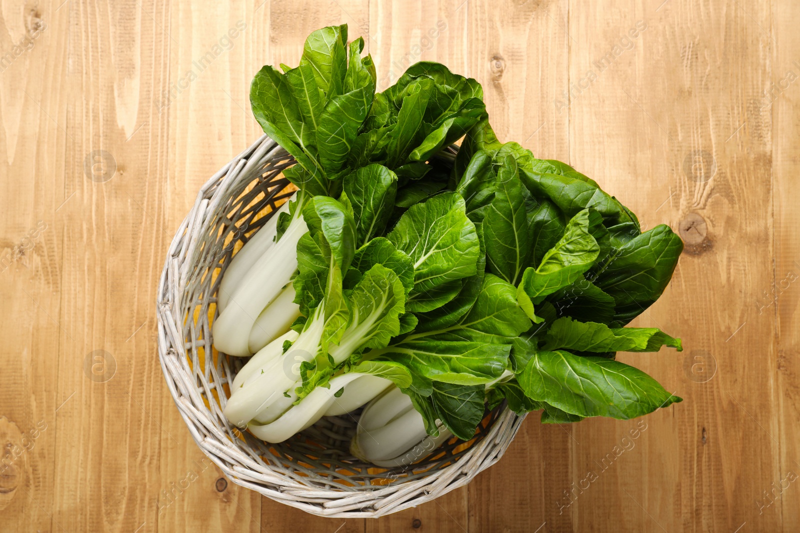 Photo of Fresh green pak choy cabbages in wicker basket on wooden table, top view