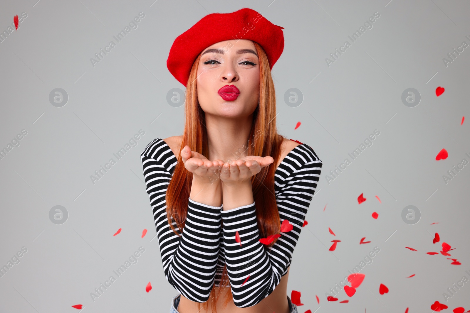 Photo of Young woman blowing kiss under heart shaped confetti on light grey background