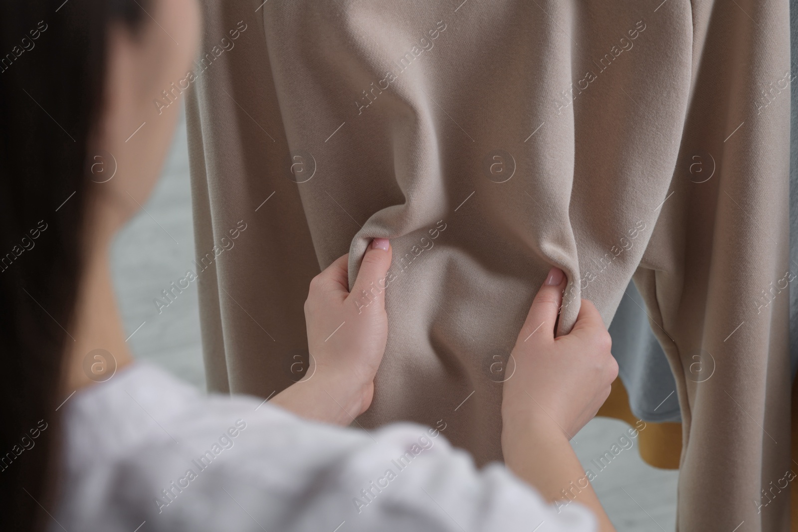 Photo of Woman touching clothes made of soft beige fabric indoors, closeup