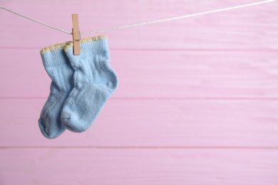 Photo of Pair of socks on laundry line against pink wooden background, space for text. Baby accessories