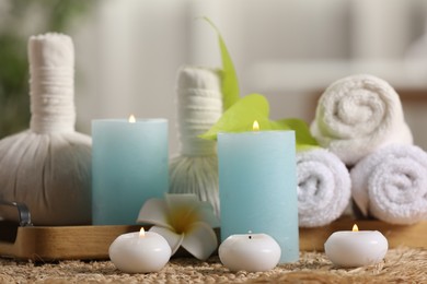 Composition with different spa products and burning candles on wicker mat, closeup