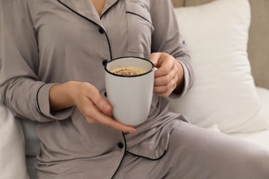 Photo of Woman in grey pajama holding cup of coffee indoors, closeup