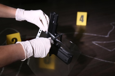 Detective putting gun into plastic bag at crime scene, closeup