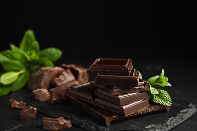 Photo of Tasty chocolate pieces and mint on black table, closeup