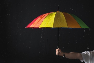 Photo of Man holding color umbrella under rain against black background, closeup