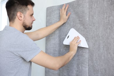 Photo of Man smoothing stylish gray wallpaper in room