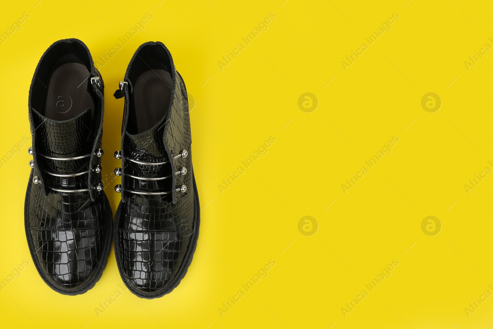 Photo of Pair of stylish ankle boots on yellow background, top view. Space for text