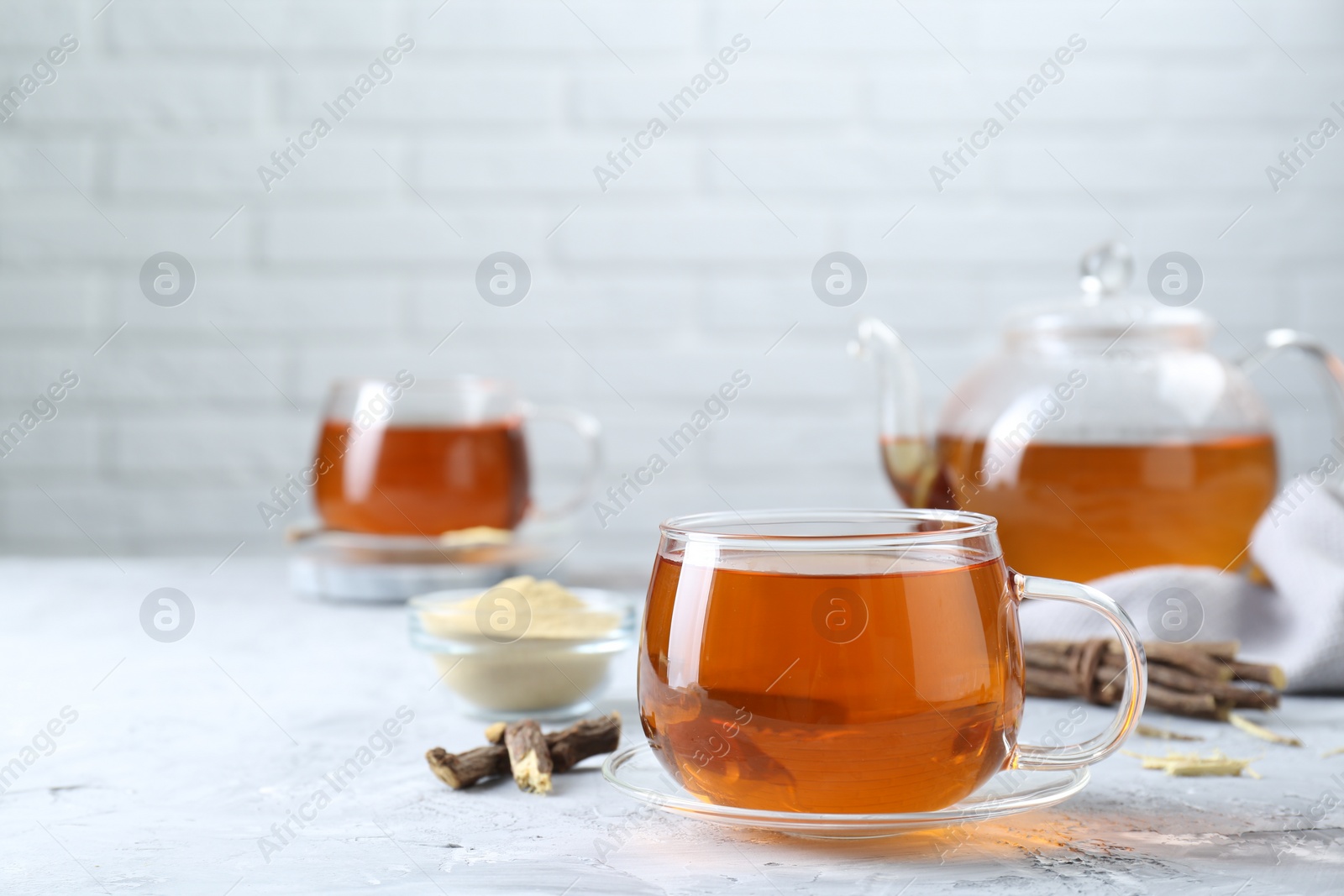 Photo of Aromatic licorice tea and dried sticks of licorice root on light gray textured table, space for text