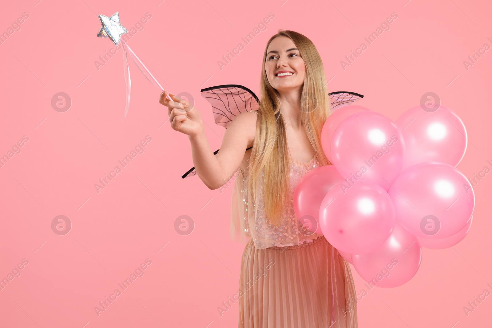 Photo of Beautiful girl in fairy costume with wings, magic wand and balloons on pink background