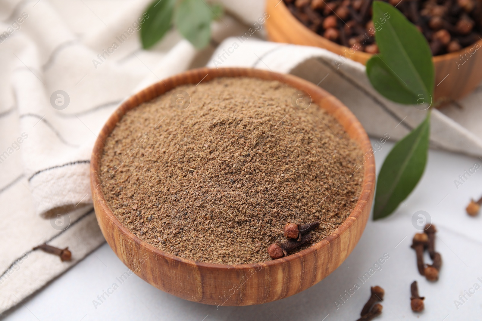 Photo of Aromatic clove powder and dried buds in bowl on white table, closeup