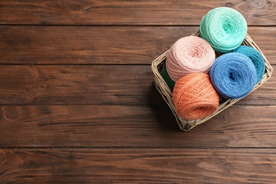 Photo of Colorful clews of threads in wicker basket on wooden table, top view. Space for text