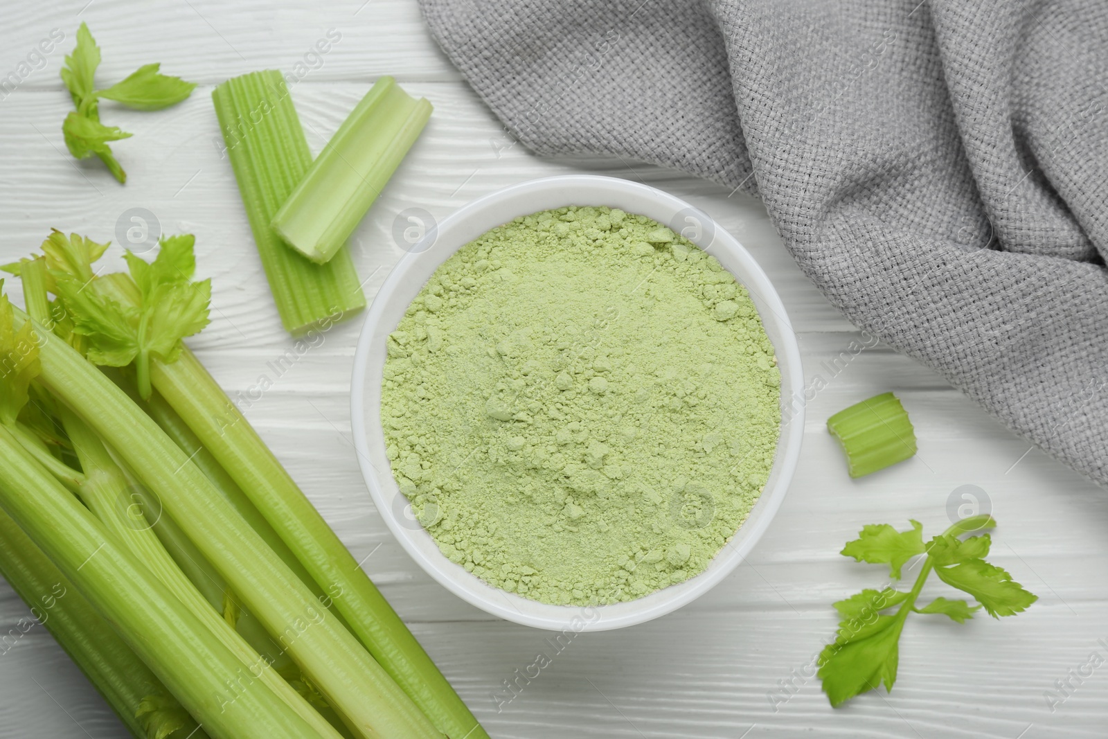 Photo of Natural celery powder in bowl and fresh stalks on white wooden table, flat lay