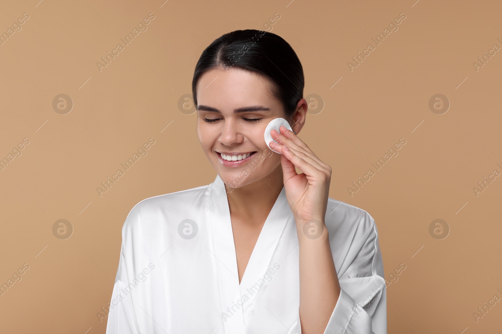 Photo of Young woman cleaning her face with cotton pad on beige background