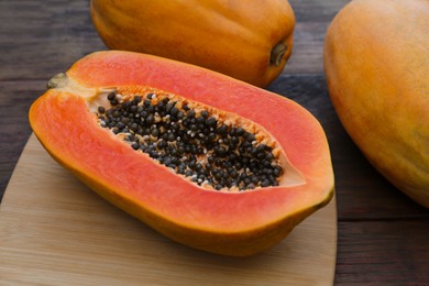 Photo of Tasty cut and whole papaya fruits on wooden table, closeup